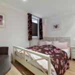 Bedroom with white bed, brown chair, and wall pictures of dogs.