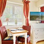 Essbereich mit Tisch, Stühlen und TV. Fenster mit roten Vorhängen.