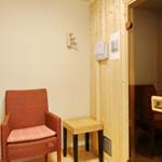 Sauna mit Holzwand und Stuhl. Draußen ein Sitzplatz mit Kissen.