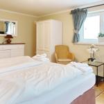 Schlafzimmer mit Bett, Schrank, Stuhl und Fenster mit Vorhängen.