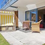 Terrasse mit Strandkorb und Sitzgruppe vor Glasfront.