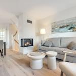 Living room with sofa, fireplace, and dining area. Wooden floor and modern furnishings.
