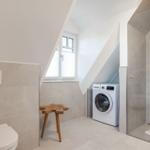 Bathroom with shower, washing machine, and toilet under sloped ceilings.