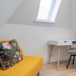 A room with a yellow sofa, a desk, and a window.