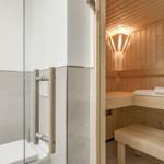 Shower with glass wall and wooden handle. Next to it, a sauna with wooden benches and towel.