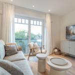 Living room with sofa, armchair, and TV. Large windows with view outside.