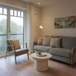 Wohnzimmer mit Sofa, Sessel und Tisch vor großem Fenster.