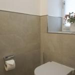 Bad mit Toilette, Toilettenpapierhalter und Blumen auf Fensterbank.