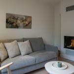 Ein grauer Sofa mit Kissen, eine Stehlampe, ein runder Tisch und ein Kamin mit brennendem Feuer.