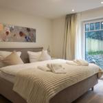 Schlafzimmer mit Doppelbett, Wandbild und Glastür zum Garten.
