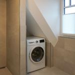 Waschmaschine unter Dachschrägen, Dusche mit Glaswand und Fenster mit Jalousie.