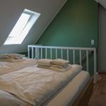 Bedroom with skylight, green wall, and wooden floor. Bed with white sheets and folded towels.