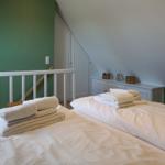 Two beds with white bedding and folded towels in an attic room with green wall.