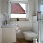 Bathroom with shower, toilet, and sink. Window with view of brick wall.