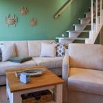 Living room with sofa, armchair, and wooden table. Green wall with crab decor. Staircase in background.