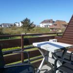 Terrace with table and chairs, view of green areas and houses.