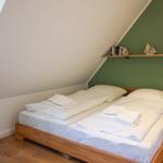 Bedroom with double bed, wooden floor, and green wall. Shelf with decorative items.