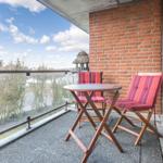 Terrace with table and two chairs with colorful cushions. View of water and trees.