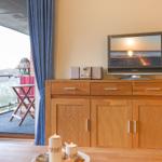 TV on wooden cabinet, balcony with chairs and table