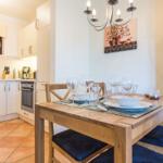 Dining area with wooden table, chairs, and set table. Kitchen in background with countertop and appliances.