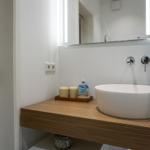 Waschbecken auf Holzunterschrank mit Spiegel und Duschbereich.