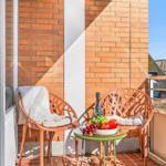 Balcony with two chairs, table, fruit, and bottle. Brick wall and thatched roofs visible.