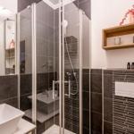 Shower cabin with glass enclosure, sink, and wooden shelf on the wall.