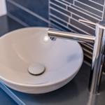 Round sink with modern faucet on dark countertop.