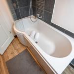 Bathtub with shower screen, two towels, and wooden floor.