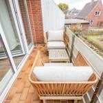 Terrace with two rattan sofas and wooden table. View of residential area with red houses.