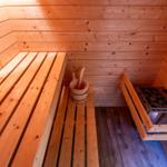 Sauna with wooden bench, bucket, and stone heater.
