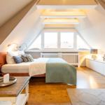 Bedroom with sloped ceilings, large window, and wooden floor.