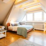 Bedroom with sloped ceiling, bed, sofa, and wooden floor.