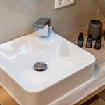 Sink with faucet on wooden vanity, three bottles and two cups.