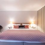 Bedroom with bed, nightstands, and lamps. Striped wall. Chair in corner.