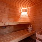 Wooden sauna with bench, bucket, and steam vent.
