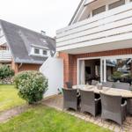 Terrace with table and chairs, garden and house with balcony.