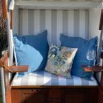 Cushion with blue pillows and floral embroidery. White glass on armrest.