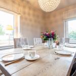 Esszimmer mit Holztisch, Stühlen und Blumendekoration.