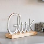 Metall-Schriftzug Gluck auf Holzsockel auf Schrank