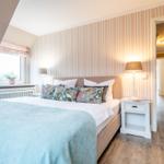 Schlafzimmer mit Bett, Nachttisch und Fenster. Wand mit Streifenmuster.