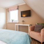 Schlafzimmer mit Bett, Kleiderschrank, Sessel und TV an der Wand.