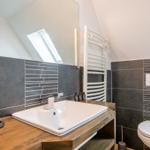 Badezimmer mit Waschbecken, Toilette und Heizkörper an schräger Decke.