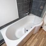 Badewanne mit Duschkabine, dunkle Fliesen und Holzboden.
