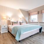 Schlafzimmer mit Bett, Nachttisch und Fenstern. Wandverkleidung und Holzboden.