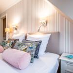 Schlafzimmer mit Bett, Kissen und Wandbeleuchtung. Streifenwand und Nachttisch.