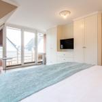 Schlafzimmer mit Bett, Schrank und TV. Große Fenster mit Blick auf Balkon.