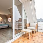 Dachgeschosszimmer mit Schlafbereich und Balkon mit Sitzgelegenheit.