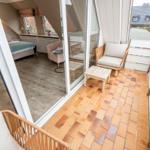 Terrasse mit Sitzgelegenheit und Blick in Schlafzimmer mit Bett und Fenstern.