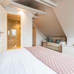 Schlafzimmer mit Dachschrägen, Bett, Sofa und Bad mit Dusche.